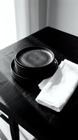 Stack of black ceramic bowls with white napkin on wooden table in minimalist interior setting, suitable for restaurant, dining, and home decor design projects.