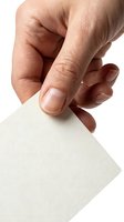 Hand holding blank white paper card between thumb and finger on white background for business presentations and mockups.