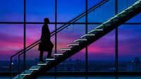 Silhouette of a woman climbing metal stairs near large windows with vibrant sunset sky and city skyline, representing ambition, career growth, and professional success.
