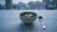Bowl of fresh salad with mixed greens, vegetables and cheese on modern table with spoon. Suitable for food blogs, healthy eating content, restaurant menus and culinary websites.