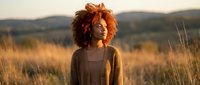 Young African American woman with curly afro hair standing in golden grassland during sunset, peaceful natural portrait for wellness and lifestyle content.