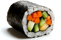 Fresh vegetable sushi roll with cucumber, carrot and avocado wrapped in nori seaweed and white rice, close-up view on white background.