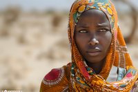 Beautiful African woman wearing traditional colorful floral headscarf in orange and yellow tones, close-up portrait against blurred desert background, perfect for cultural and fashion projects.