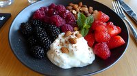 Fresh mixed berries with whipped cream, mint leaves and crushed almonds served on dark plate, healthy dessert composition on wooden table surface.