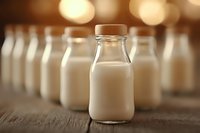 Fresh milk bottles arranged in row on rustic wooden table with warm bokeh background lighting creating cozy atmosphere for dairy product marketing.
