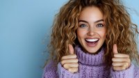 Young Caucasian woman with curly blonde hair wearing purple knit turtleneck sweater showing thumbs up and expressing joy against blue background.