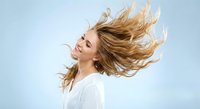 Young blonde woman with flowing hair in motion against blue sky background expressing freedom and joy in white clothing for lifestyle photography.