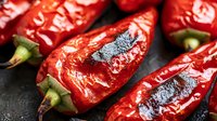 Roasted red peppers with charred skin and green stems on dark surface, ready for cooking and culinary preparations.