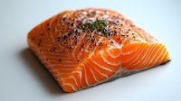 Fresh raw salmon fillet with black pepper and herbs on white background, close up view showing marbled texture and vibrant orange color. Suitable for cooking blogs.