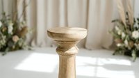 Rustic wooden pedestal stand in a bright studio with floral decor, casting soft shadows on a white floor for elegant event styling.