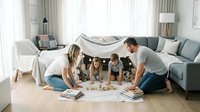 Happy Caucasian family with two children playing board games together on living room floor under blanket fort made from couch cushions and sheets.
