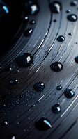Water drops on dark textured surface with blue reflections create dramatic macro photography composition showing surface tension and hydrophobic effect.