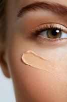 Close-up of brown eye with long lashes and foundation cream sample on smooth skin, demonstrating makeup application and skincare routine for beauty industry.