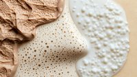 Creamy beige foam texture with golden dots pattern alongside textured fabric materials on neutral background for cosmetic and skincare product design applications.