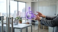 Hand pointing at wheelchair accessibility symbol on glass door in modern office with city skyline view, representing inclusive workplace design and ADA compliance.