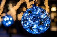 Blue glass Christmas ornament with LED lights creating magical bokeh effect against warm holiday background for festive decorations and seasonal designs.