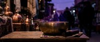 Steaming bowl of traditional food on wooden table during evening street market with purple twilight sky and blurred crowd background creating atmospheric dining scene.