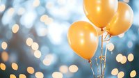 Orange helium balloons floating against blurred bokeh background with soft blue tones and glowing lights creating festive celebratory atmosphere.