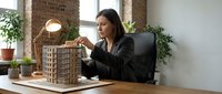 Woman architect reviewing architectural model in modern office with plants and brick walls, suitable for business and design projects.