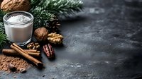 Glass of milk with cinnamon sticks, walnuts, cocoa powder and pine branches on dark stone background with copy space. Winter holiday drink concept.