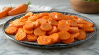 Fresh sliced carrots on gray ceramic plate against marble background, bright orange vegetable circles arranged in layers, healthy cooking ingredient.