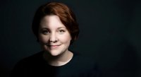 Professional young woman with short auburn hair smiling confidently in dark sweater against black background for corporate headshot and business portrait.