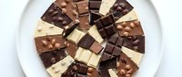 Assorted chocolate pieces arranged on white plate, including dark, milk, and white varieties with nuts, perfect for confectionery, food photography, and culinary design projects.