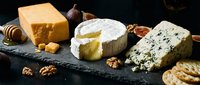 Gourmet cheese platter with aged cheddar, creamy brie, blue cheese, walnuts, figs and honey on dark slate board for wine tasting and appetizer presentations.