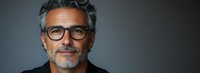 Confident mature man with gray hair, beard and glasses smiling against dark background. Professional portrait showing wisdom and experience. Successful businessman concept.