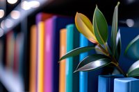 Green plant leaves against colorful book spines on bookshelf with soft bokeh background creates peaceful library or study atmosphere.