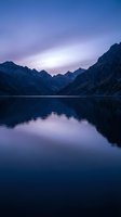 Serene mountain lake at twilight with purple sky reflection and dramatic peaks creating peaceful landscape for meditation and wellness content.