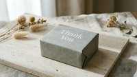 Gray kraft paper gift box with Thank You text on wooden board, surrounded by dried flowers, elegant packaging for special occasions.