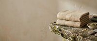 Folded beige towels stacked on rustic stone surface with spa essentials, suitable for wellness, hospitality and bathroom design projects.