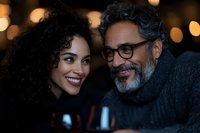 Happy mature mixed-race couple sharing intimate moment in cozy restaurant setting with warm bokeh lights creating romantic atmosphere for date night.