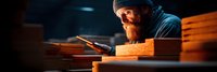 Skilled bearded craftsman working with hammer and chisel on wood in dimly lit workshop. Traditional woodworking and carpentry craftsmanship concept.