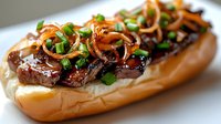 Juicy teriyaki beef sandwich topped with caramelized onions and fresh green onions on a soft bun, served on a white plate.