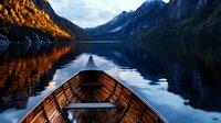 Wooden boat bow on tranquil mountain lake at sunset, dramatic alpine landscape with snow peaks reflected in calm water, golden autumn trees on rocky shore.