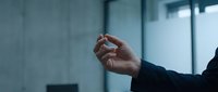 Businessman in dark suit making fist gesture indoors with modern office background, expressing determination, strength, motivation or power in corporate environment.