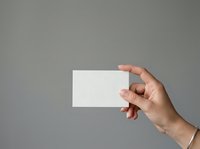 Hand holding blank white card against neutral gray background, suitable for business card mockups, branding presentations, and promotional material design.