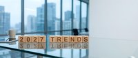 Wooden blocks spelling 2027 TRENDS on modern office desk with city skyline view through large windows for business planning and forecasting concepts.