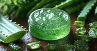 Fresh aloe vera gel in glass jar with cut pieces of natural plant leaves on wooden surface, moisturizing skincare and wellness concept.