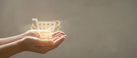 Close-up of open hand holding glowing shopping cart icon against neutral background, representing e-commerce, online retail, digital shopping, and consumer commerce solutions.