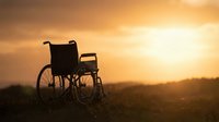 Silhouette of empty wheelchair in golden sunset field, symbolizing hope, recovery, and resilience for healthcare and wellness design projects.