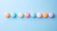 Colorful macarons arranged in straight line on pastel blue background. Sweet French desserts in soft pastel colors creating minimal composition.
