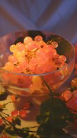 Fresh translucent white grapes in glass bowl illuminated by warm orange light, creating glowing effect against soft purple background.