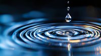 Water drop falling into calm surface creating concentric ripples with blue tones and orange reflections, captured in macro photography with shallow depth of field.
