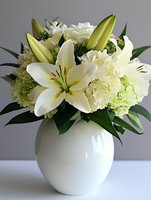 Elegant white lily and hydrangea flower arrangement in round ceramic vase against neutral background, featuring fresh blooms and green foliage for wedding decor.