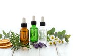 Essential oils in glass dropper bottles with fresh herbs and flowers on white wooden background for aromatherapy and natural wellness treatments.