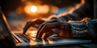 Hands typing on laptop keyboard in warm evening light with cozy knitted sweater sleeves, creating atmospheric workspace scene for remote work and productivity.