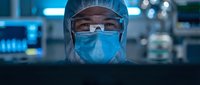 Medical professional in protective equipment working at computer in modern healthcare facility with advanced technology and monitoring systems.